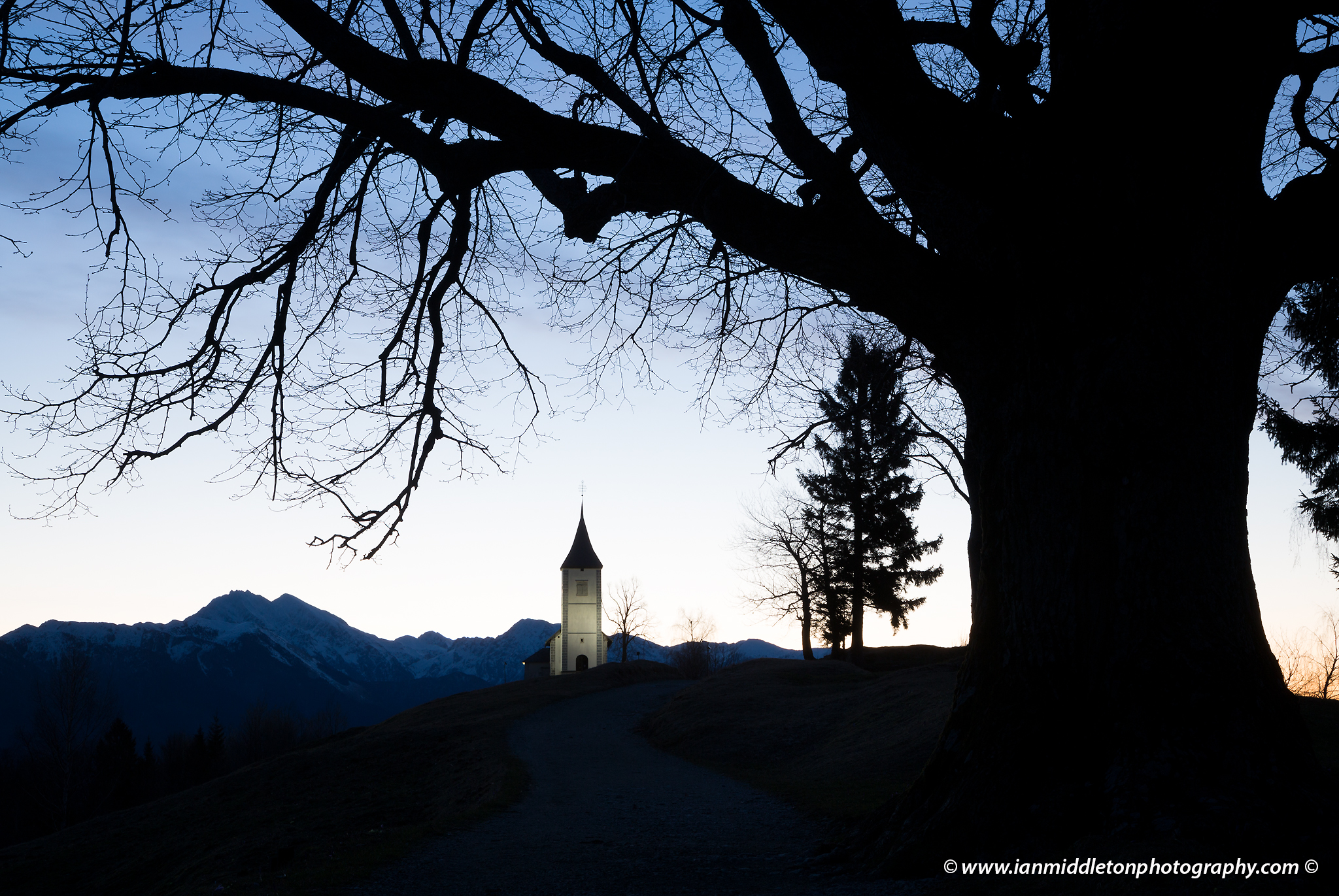 Jamnik church of Saints Primus and Felician, perched on a hill on the Jelovica Plateau with the kamnik alps and Storzic mountain in the background, Slovenia.