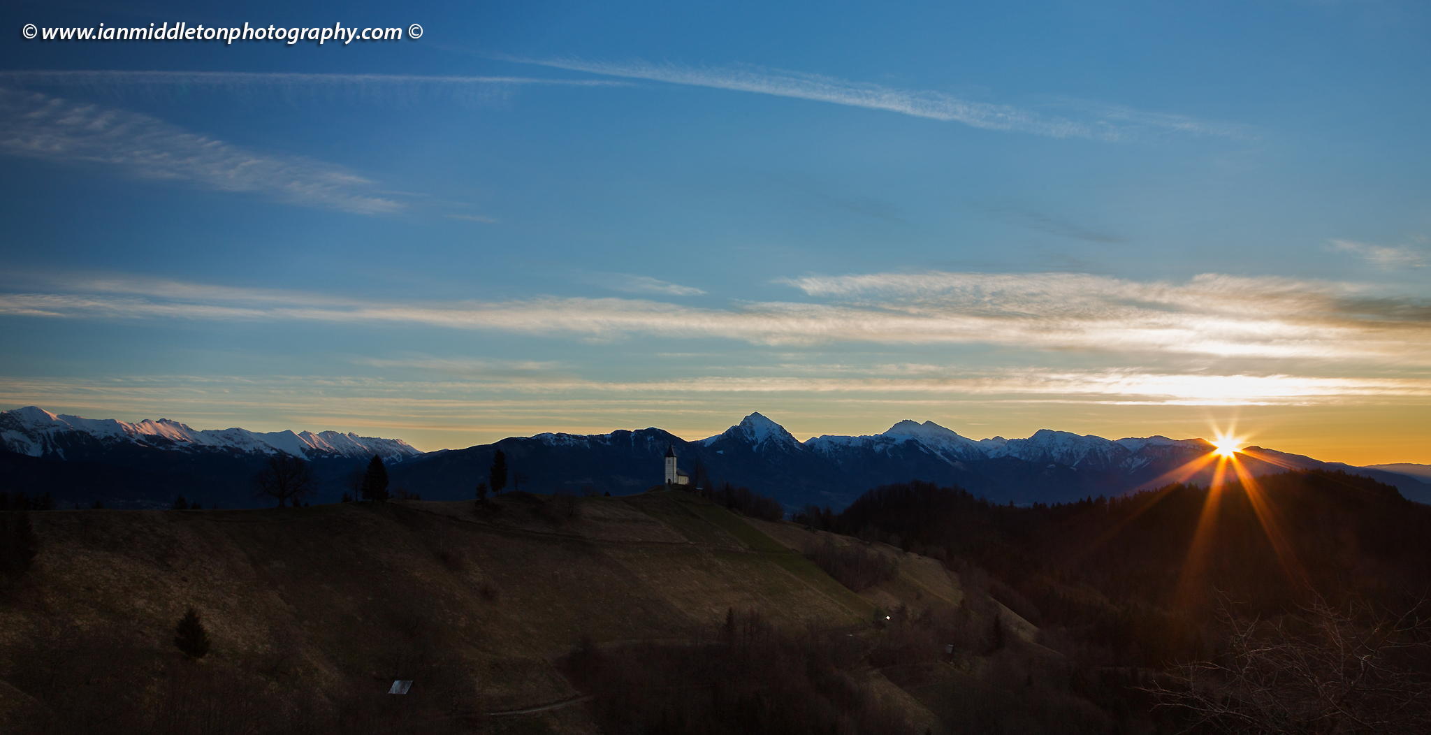 Jamnik church of Saints Primus and Felician at sunrise, perched on a hill on the Jelovica Plateau with the kamnik alps and storzic mountain in the background, Slovenia.
