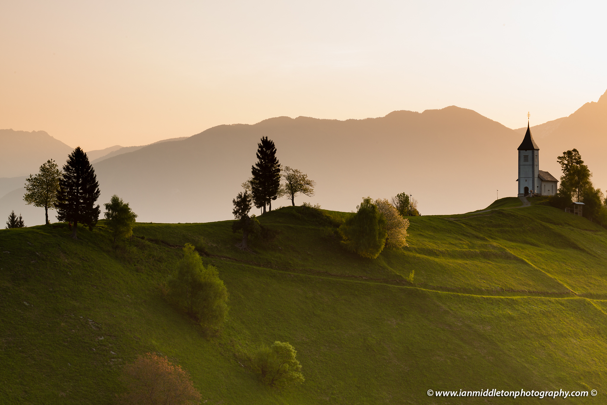 Jamnik church of Saints Primus and Felician at sunrise, perched on a hill on the Jelovica Plateau with the kamnik alps and storzic mountain in the background, Slovenia.