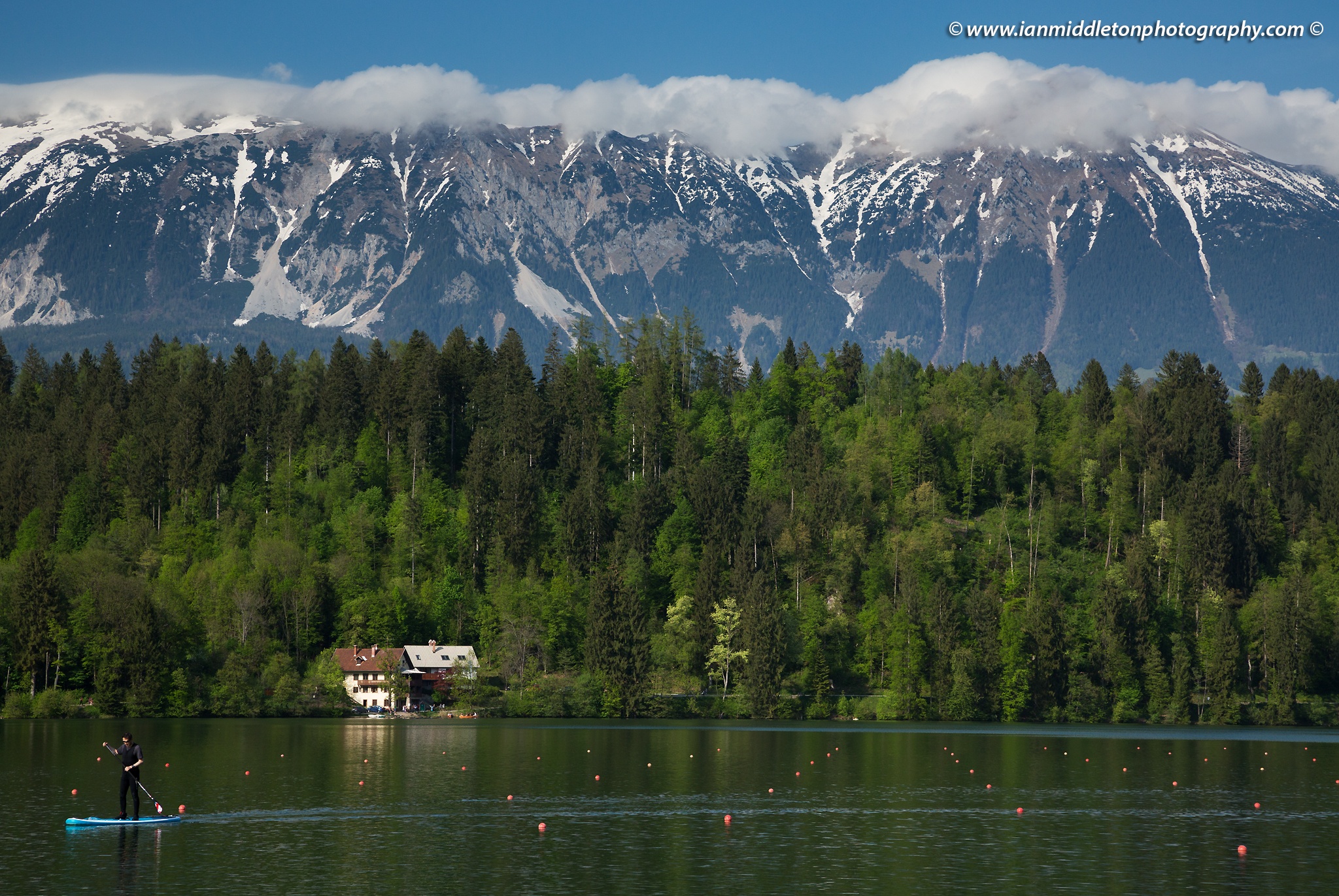 Man standup paddleboarding (SUP) on Lake Bled, Slovenia with the Karavanke Mountains in the background.