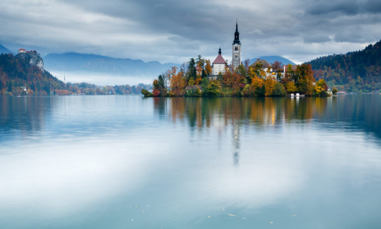 View across Lake Bled to the island church and clifftop castle in all it's autumn glory, Slovenia.
