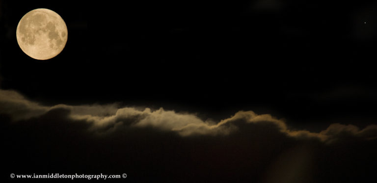 Full moon setting over clouds