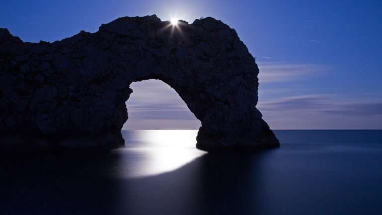 Durdle Door in the moonlight, Dorset, England. Captured late evening as the moonlight flooded through the rock's archway. The long exposure has also produced some nice star trails to the right of the arch. Durdle door is one of the many stunning locations to visit on the Jurassic coast in southern England.