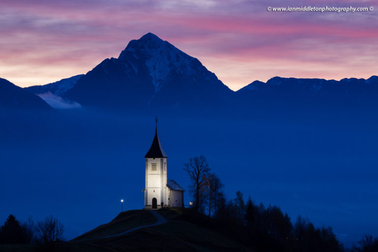 Jamnik church of Saints Primus and Felician at sunrise, perched on a hill on the Jelovica Plateau with the kamnik alps and storzic mountain in the background, Slovenia.