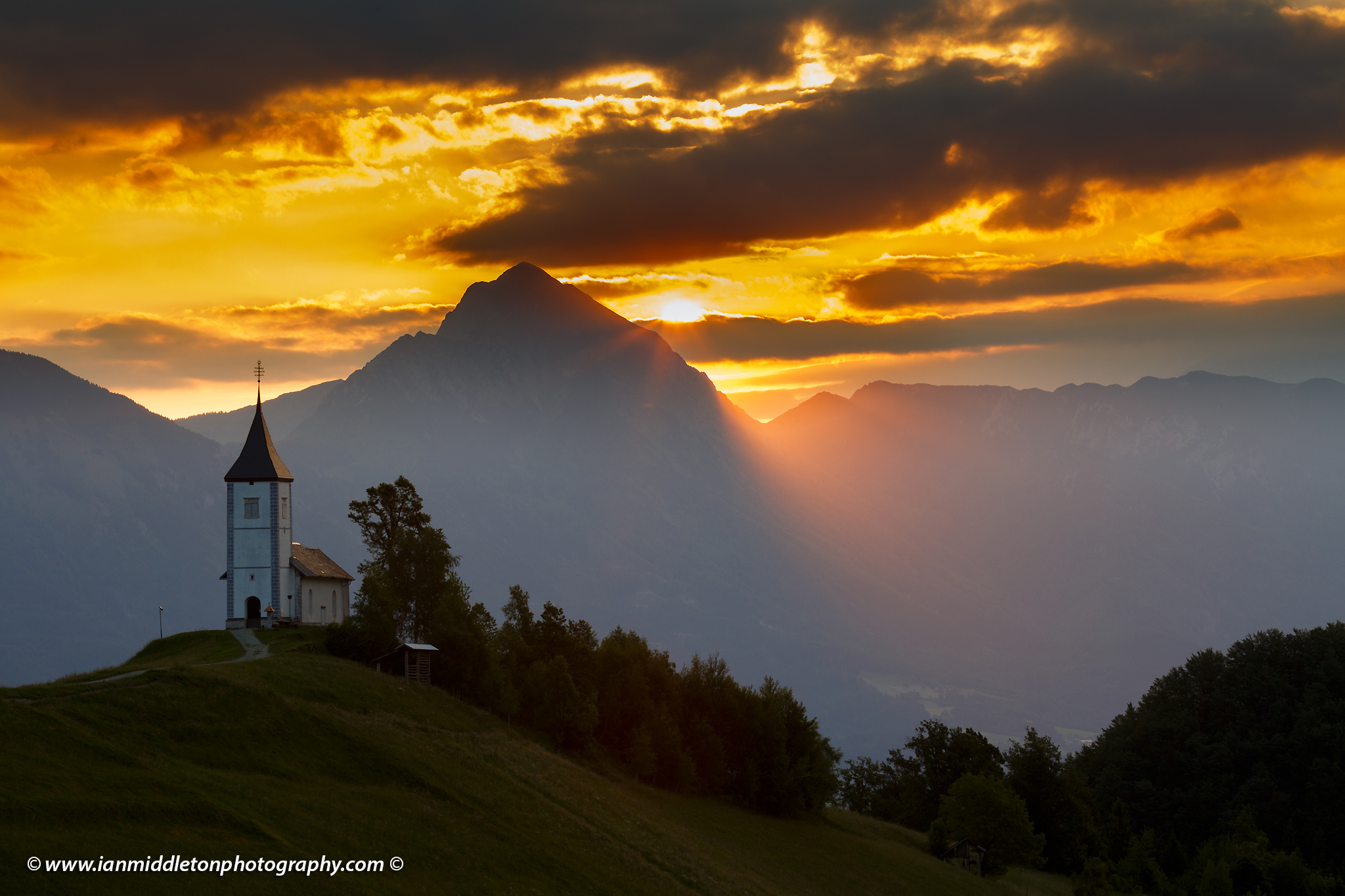 Jamnik church of Saints Primus and Felician at sunrise, perched on a hill on the Jelovica Plateau with the kamnik alps and storzic mountain in the background, Slovenia.