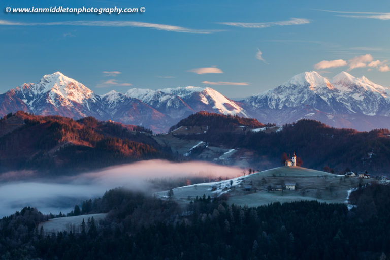 View at sunrise in winter from Rantovše hill across to Sveti Tomaz nad Praprotnim (church of Saint Thomas) and the Kamnik Alps, Slovenia.