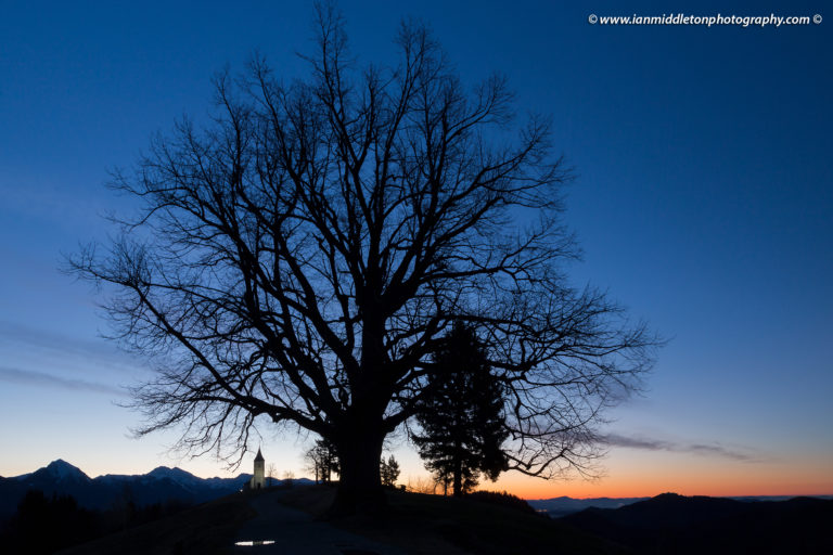 Jamnik church of Saints Primus and Felician at dawn, perched on a hill on the Jelovica Plateau with the kamnik alps and storzic mountain in the background, Slovenia.