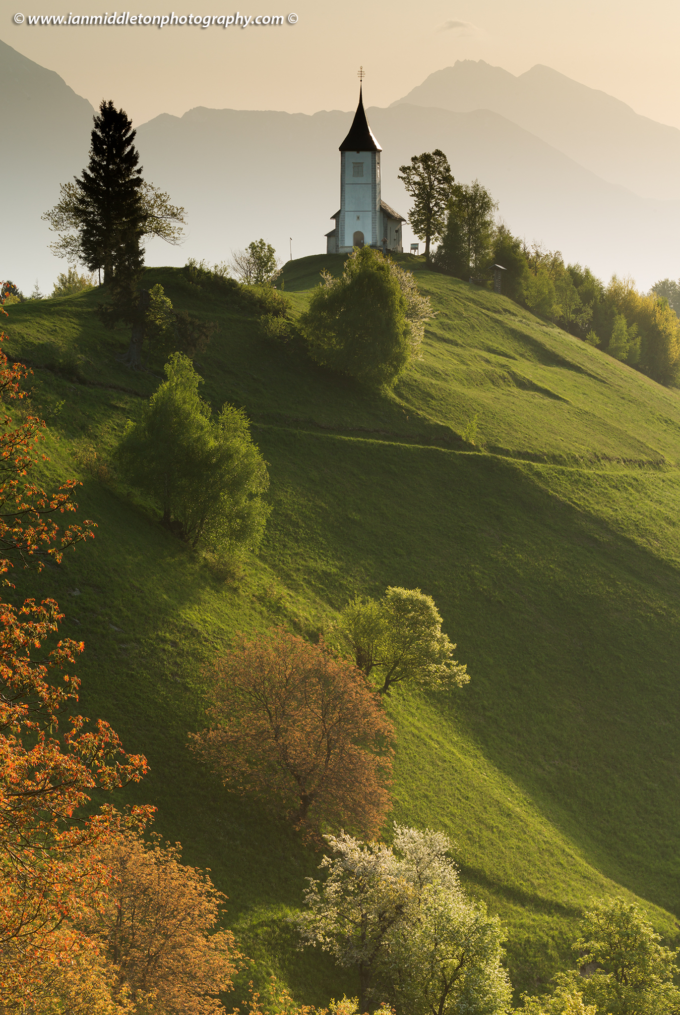 Jamnik church of Saints Primus and Felician, perched on a hill on the Jelovica Plateau with the kamnik alps and Storzic mountain in the background, Slovenia.