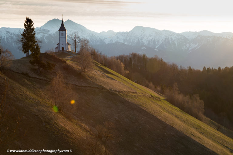 Jamnik church of Saints Primus and Felician, perched on a hill on the Jelovica Plateau with the kamnik alps and Storzic mountain in the background, Slovenia.