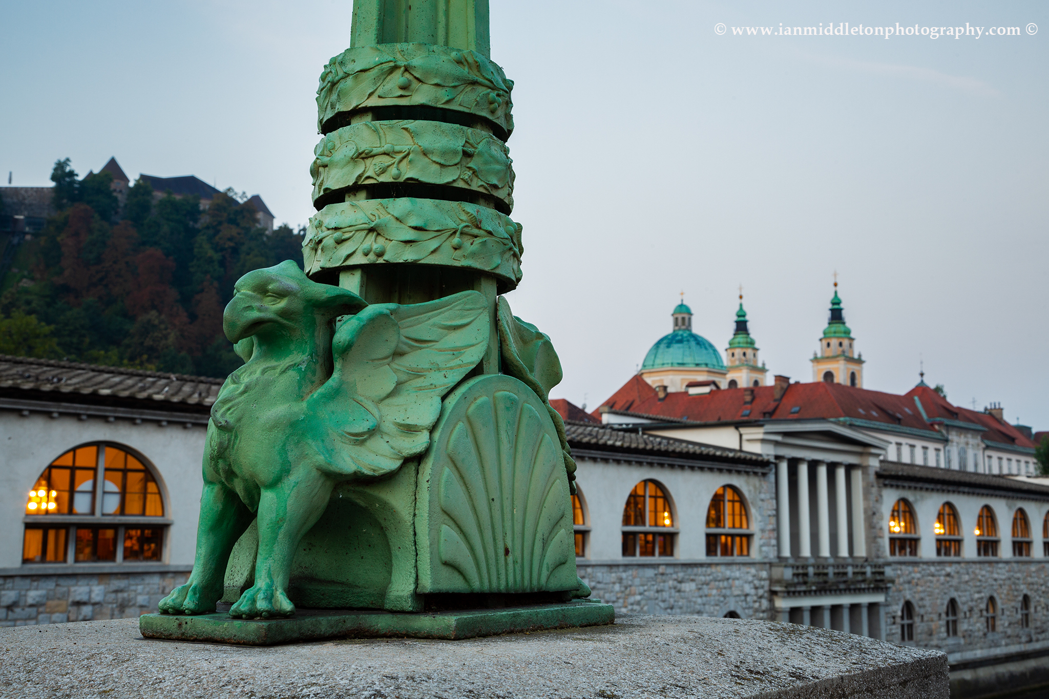 Ljubljana Dragon Bridge Griffin with castle, marketplace and cathedral of Saint Nicholas in the background, Slovenia.