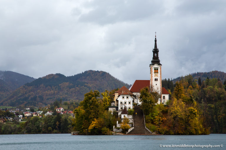 Tourist walking up the steps of Lake Bled's island church on a rainy autumn morning, Slovenia.