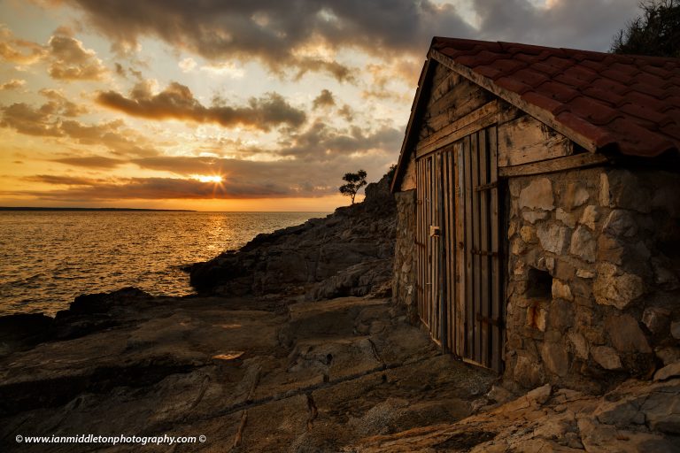 Sunrise over a boathouse on Zaosiri Beach on the coastal area of Cunski, which lies just 8kms north of Mali Losinj on Losinj Island, Croatia. The strip of land to the left is Punta Kriza.