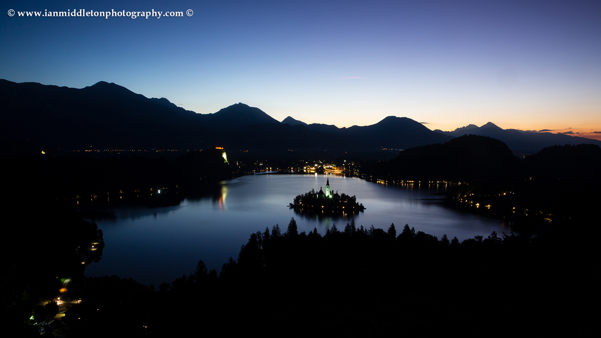 View across Lake Bled to the island church and clifftop castle from Ojstrica at dawn, Slovenia.