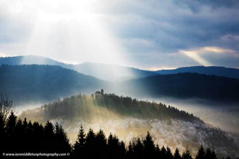 Afternoon sunrays falling over the church of Sveti Josef (Saint Joseph) seen from the church of Saint Anna (Sveta Ana). Sveta Ana is perched upon an exposed hill overlooking the Ljubljansko Barje (Ljubljana marsh) near the village of Preserje.