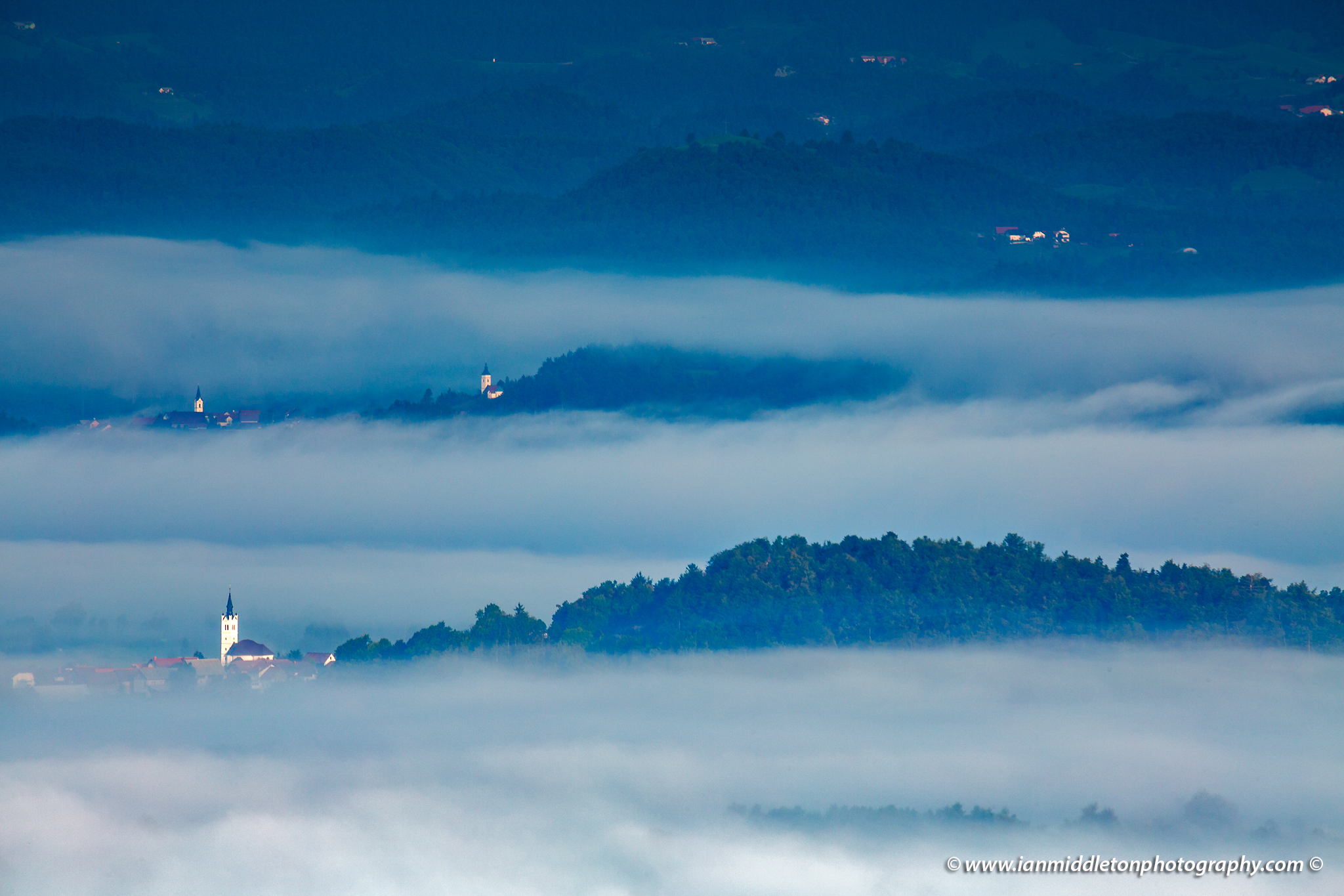 Mist in the valley enshrouding the many churches on the Ljubjana Moors in the morning, Slovenia. Seen from the church of Saint Anna (Sveta Ana). Sveta Ana is perched upon an exposed hill overlooking the Ljubljansko Barje (Ljubljana marsh) near the village of Preserje.