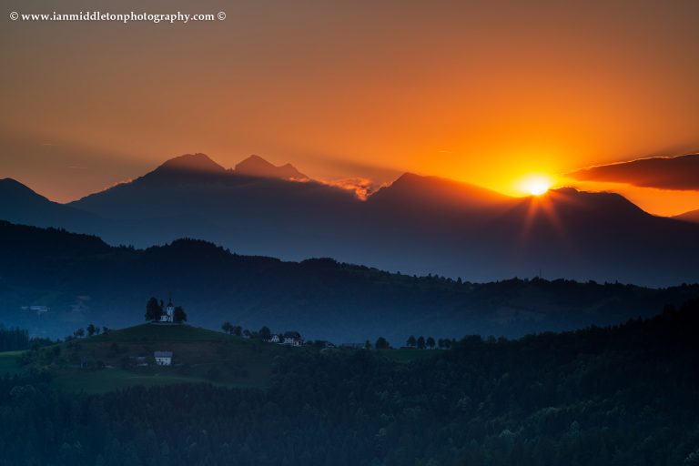 View at sunrise from Rantovše hill across to Sveti Tomaz nad Praprotnim (church of Saint Thomas) and the Kamnik Alps, Slovenia. What to photograph in the summer.