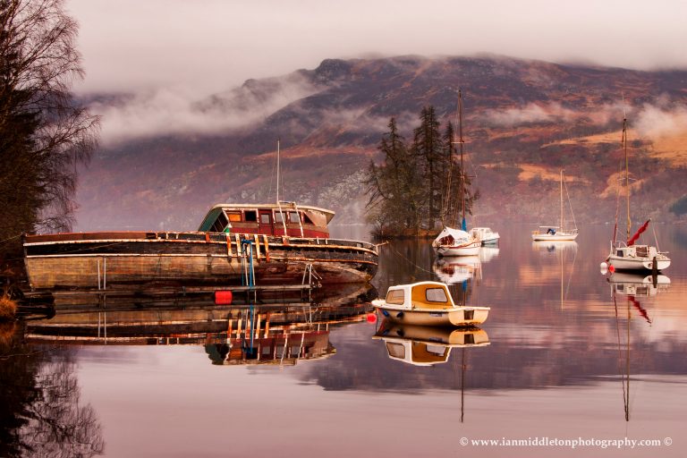 Misty morning reflections of Loch Ness in Scotland. Boats reflected as the morning mist dissipates near Fort Augustus.