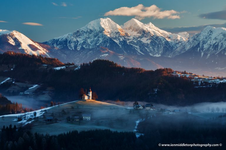 View at sunrise in winter from Rantovše hill across to Sveti Tomaz nad Praprotnim (church of Saint Thomas) and the Kamnik Alps, Slovenia.