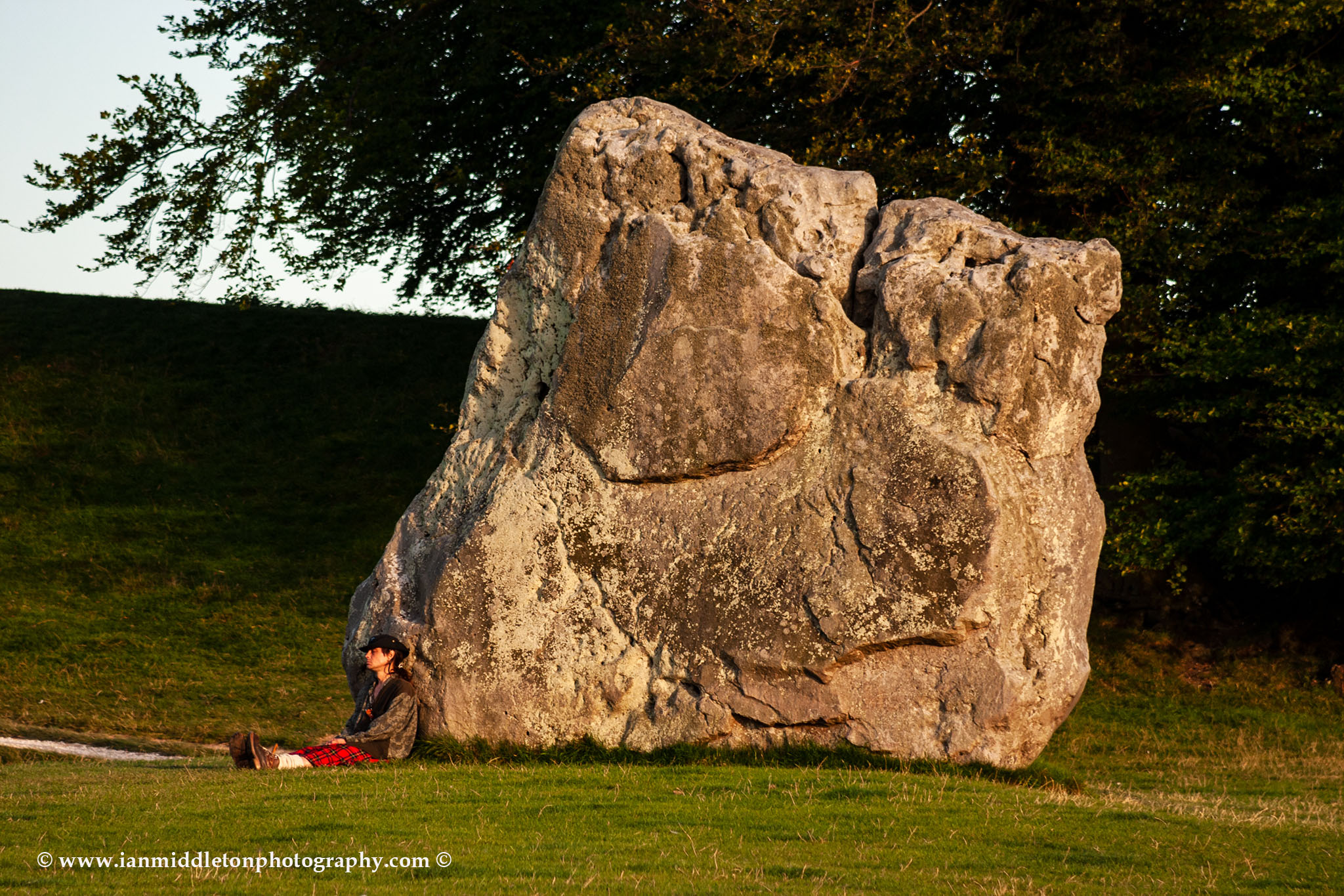 Man in kilt resting against a stone at Avebury Stone Circle in Wiltshire, England.