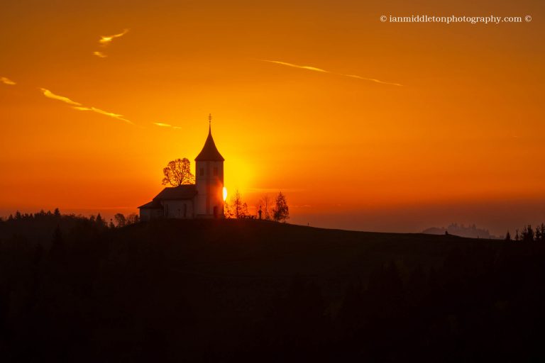 Jamnik church of Saints Primus and Felician at sunrise with the twin spires of Sveti Jost in the distance. This church is perched on a hill on the Jelovica Plateau, Slovenia.