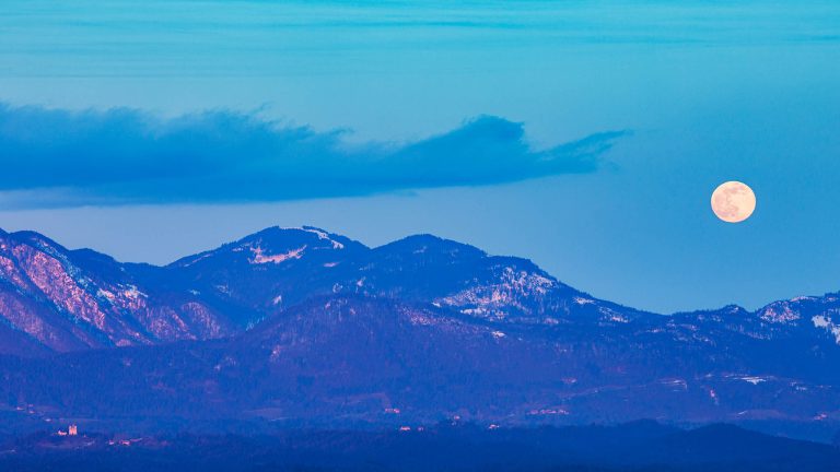 Full moon rising over the edge of the Kamnik Alps behind Tunjice church, Slovenia.