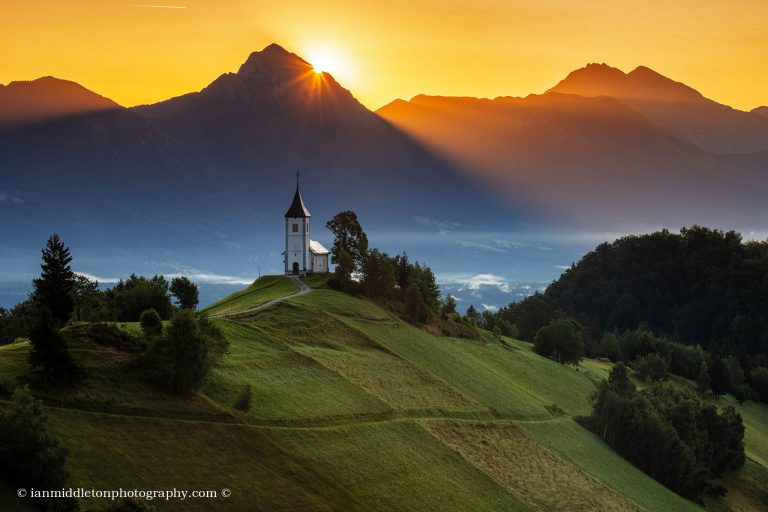 Jamnik church of Saints Primus and Felician at sunrise, perched on a hill on the Jelovica Plateau with the kamnik alps and storzic mountain in the background, Slovenia.