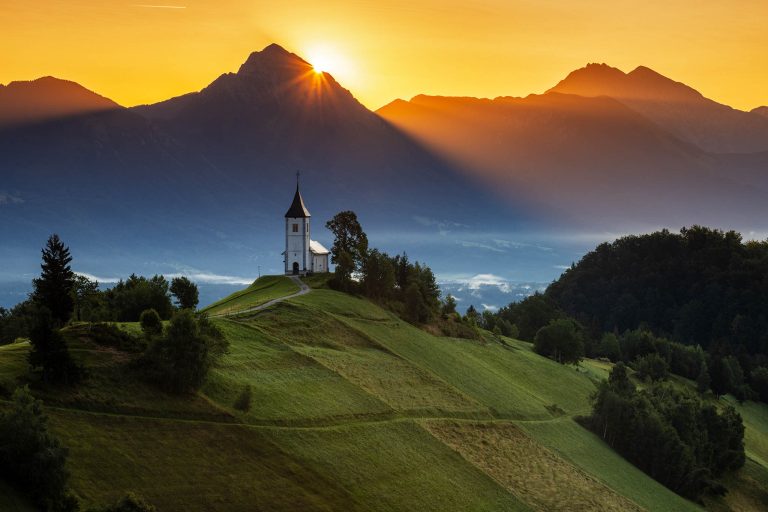 Jamnik church of Saints Primus and Felician at sunrise, perched on a hill on the Jelovica Plateau with the kamnik alps and storzic mountain in the background, Slovenia.