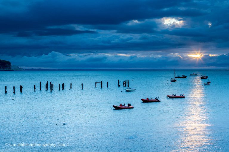 Sun rising at Swanage old pier with Old Harry Rocks in the background, Dorset, England.