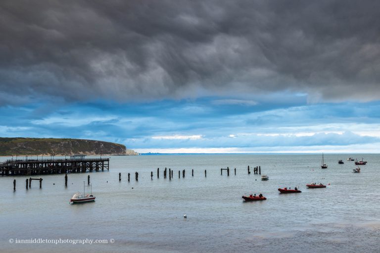 Storm over the old pier in Swanage with Old Harry Cliffs in the background, Dorset, England.