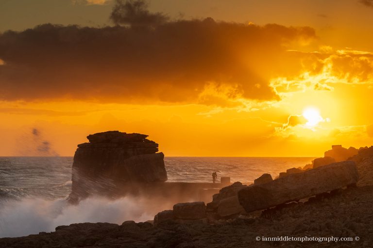 Waves crashing over Pulpit rock at sunset and the promontary at Portland Bill, near Weymouth, Jurassic Coast, Dorset, England. Pulpit Rock is an artificial stack that was left behind after quarrymen dug away a natural arch in 1870s. The Jurassic Coast is a stretch of coastline with a geology that dates back 185 million years, and is a UNESCO World Heritage Site.