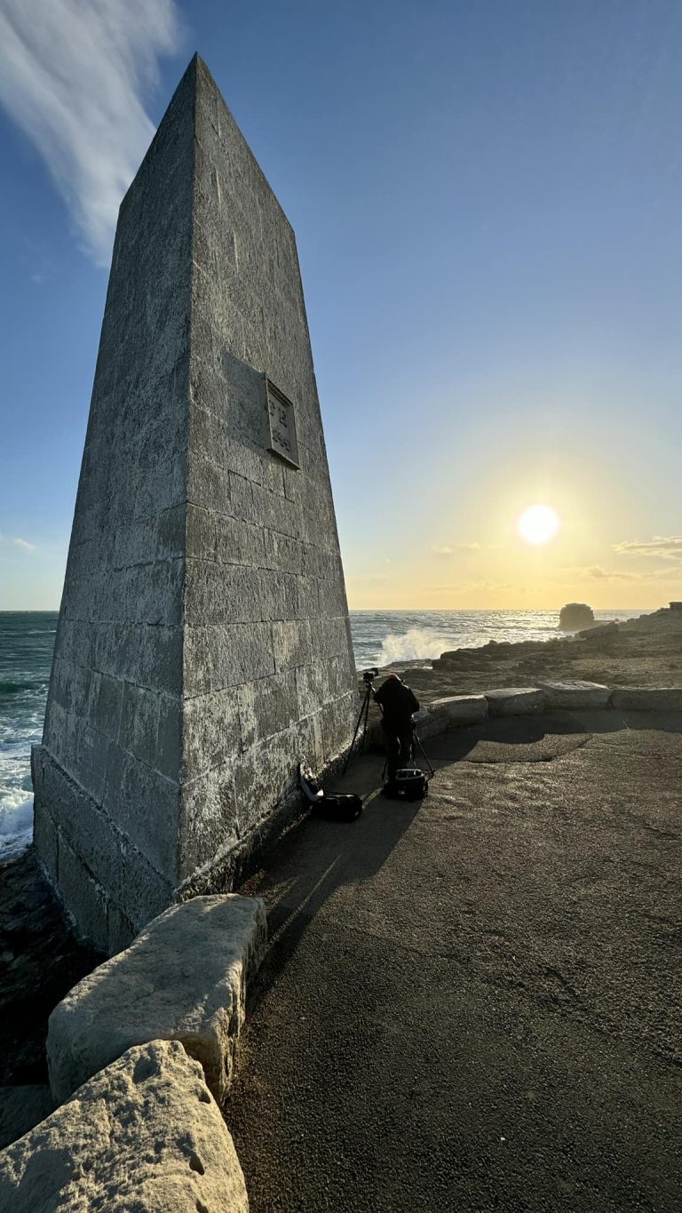 Using the The Trinity Obelisk, a triangular pillar of white Portland stone, at Portland Bill as a shelter from the relentless wind while photographing the sunset.