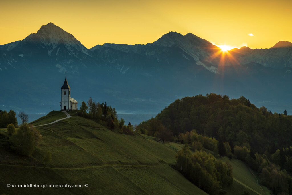 Jamnik church of Saints Primus and Felician at sunrise, perched on a hill on the Jelovica Plateau with the kamnik alps and storzic mountain in the background, Slovenia.