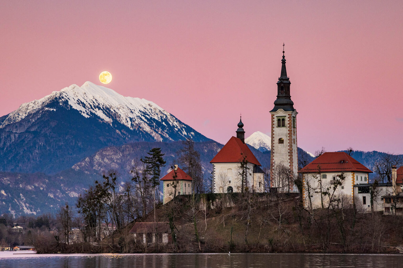 Full moon (January Wolf Moon) rising over Veliki Vrh mountain peak at sunset beside the island church at Lake Bled, Slovenia. Taken on 13th January during the major lunar standstill of 2025