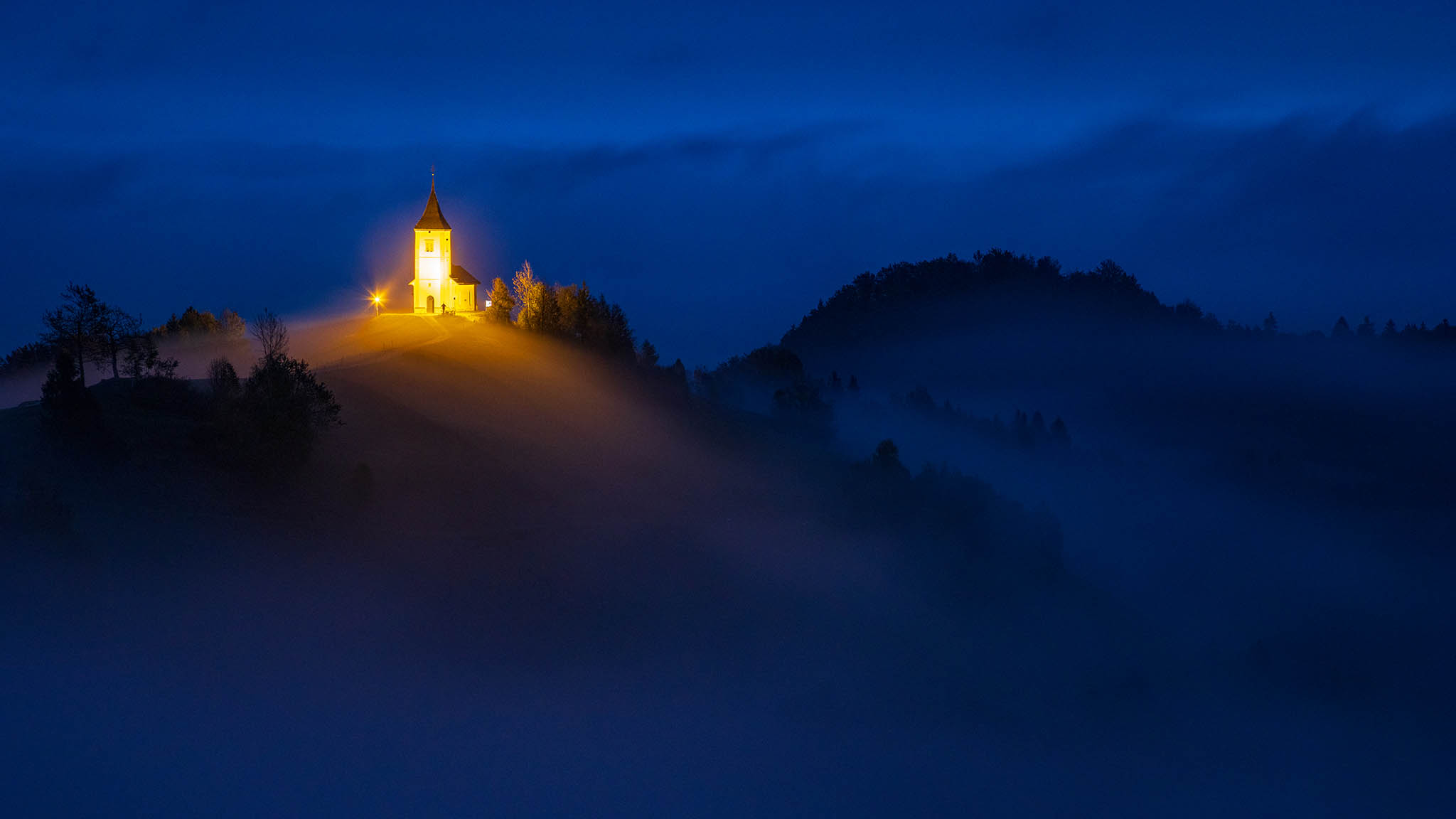 Jamnik church of Saints Primus and Felician at dawn surrounded by mist, perched on a hill on the Jelovica Plateau, Slovenia.