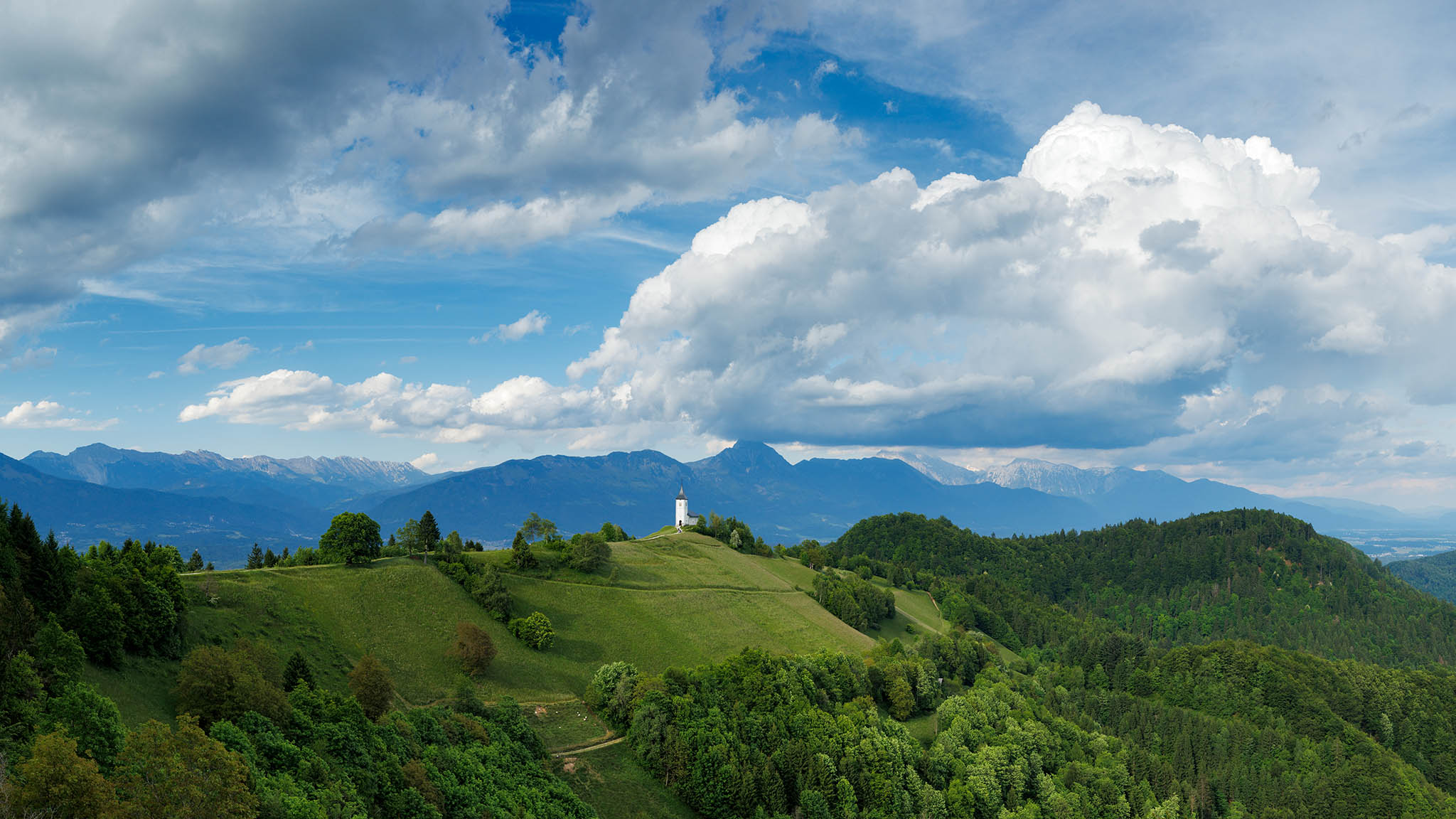 Stitched panorama of Jamnik church of Saints Primus and Felician, perched on a hill on the Jelovica Plateau with the kamnik alps and Storzic mountain in the background, Slovenia.