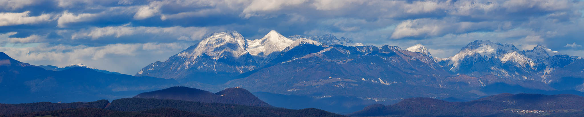 View across to the entire Kamnik Alps, Slovenia. A stitched panorama made from 7 photos. Some prominent mountain peaks from left to right are Stožič, Kočna, Grintovec, Skuta, Zahodni Vrh, Lučka Baba, Ojstrica. You can also see Smlednik Castle and the Church of Mary on Šmarna Gora, just below Grintovec and Kočna.