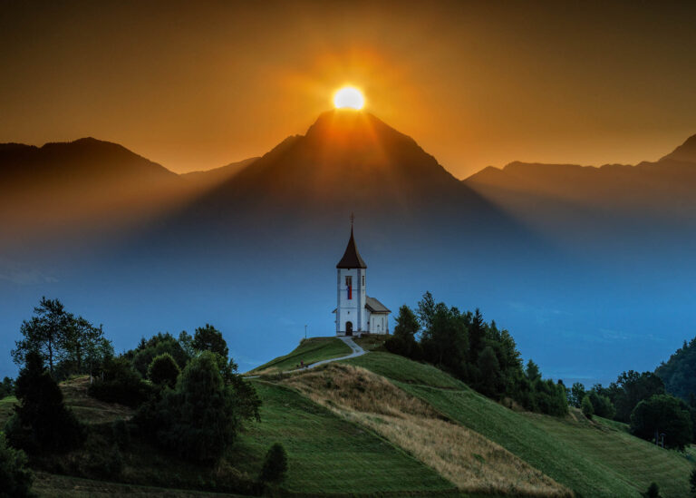 Jamnik church of Saints Primus and Felician as the sun rises over the peak of storzic mountain, part of the Kamnik Alps, Slovenia.
